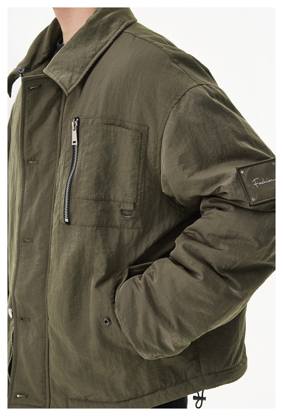 Close-up of the olive jacket showing its zip chest pocket, D-ring, sleeve patch and snap-front closure.