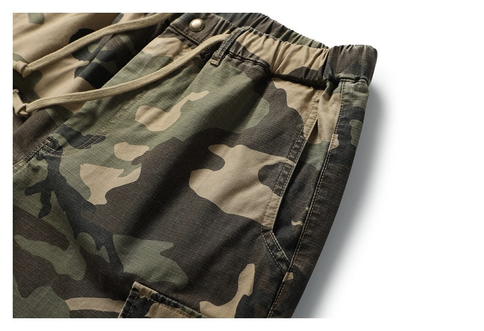 Angled close-up of the camouflage shorts' elastic waistband, drawstring, side pocket, and stitching.