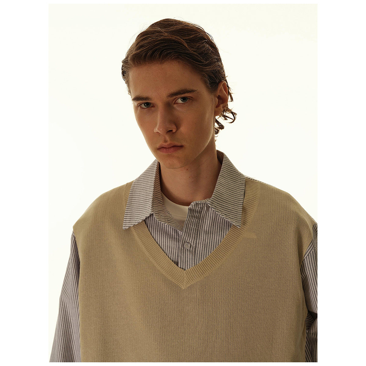 Close-up of a model wearing a tan V-neck sweater vest over a gray striped collared shirt.