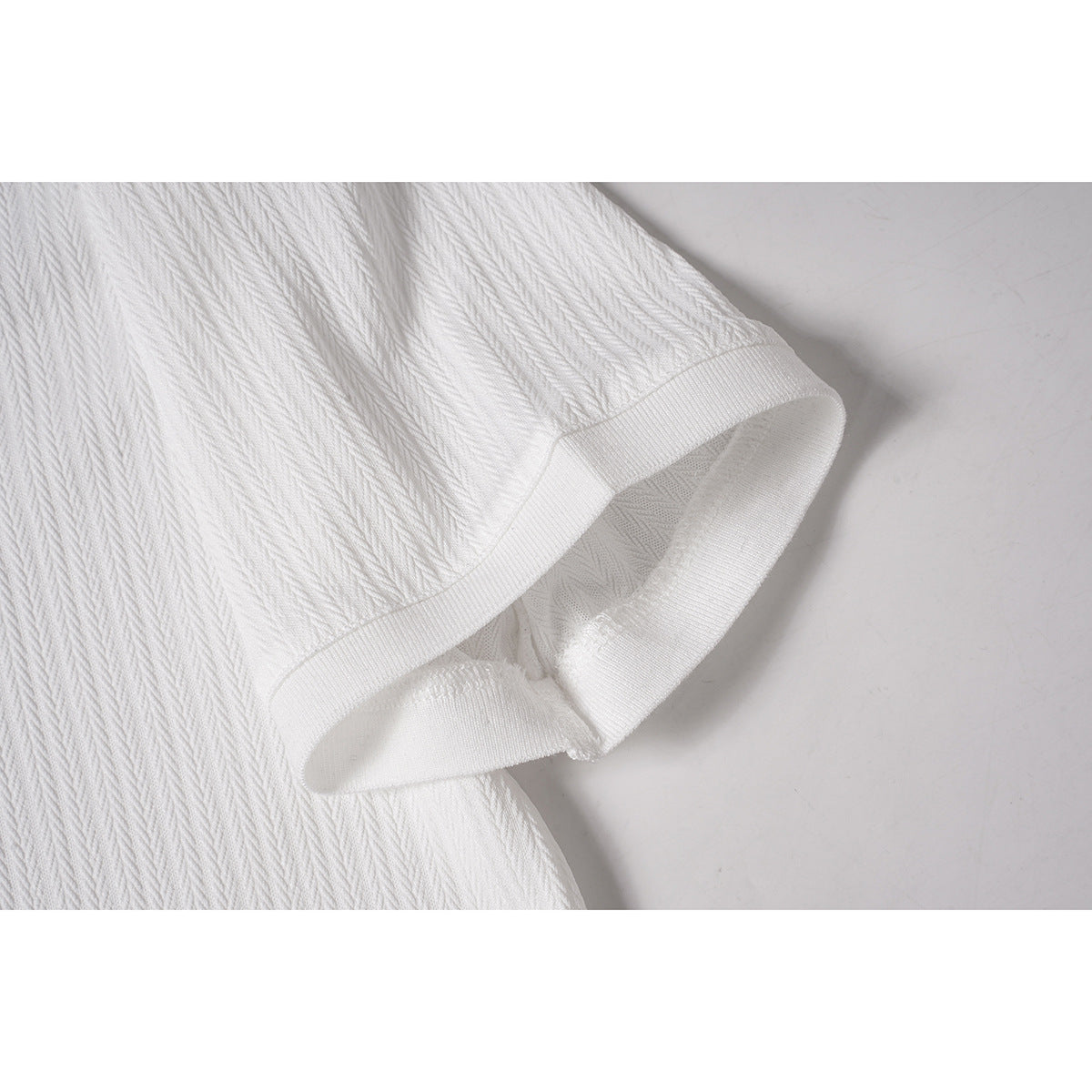 Close-up of a white polo shirt's short sleeve and ribbed cuff, with a subtle textured pattern.