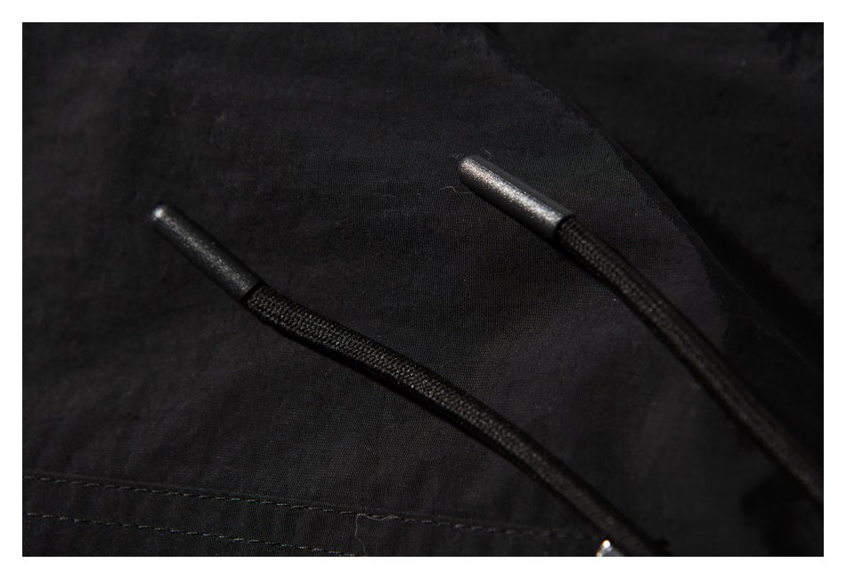 Close-up of two black drawstrings with metallic tips against black garment fabric.