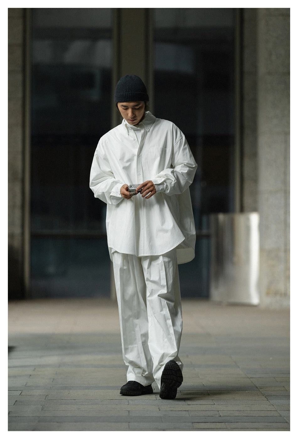 Model wearing an oversized white button-front shirt and matching wide-leg trousers with a black beanie.