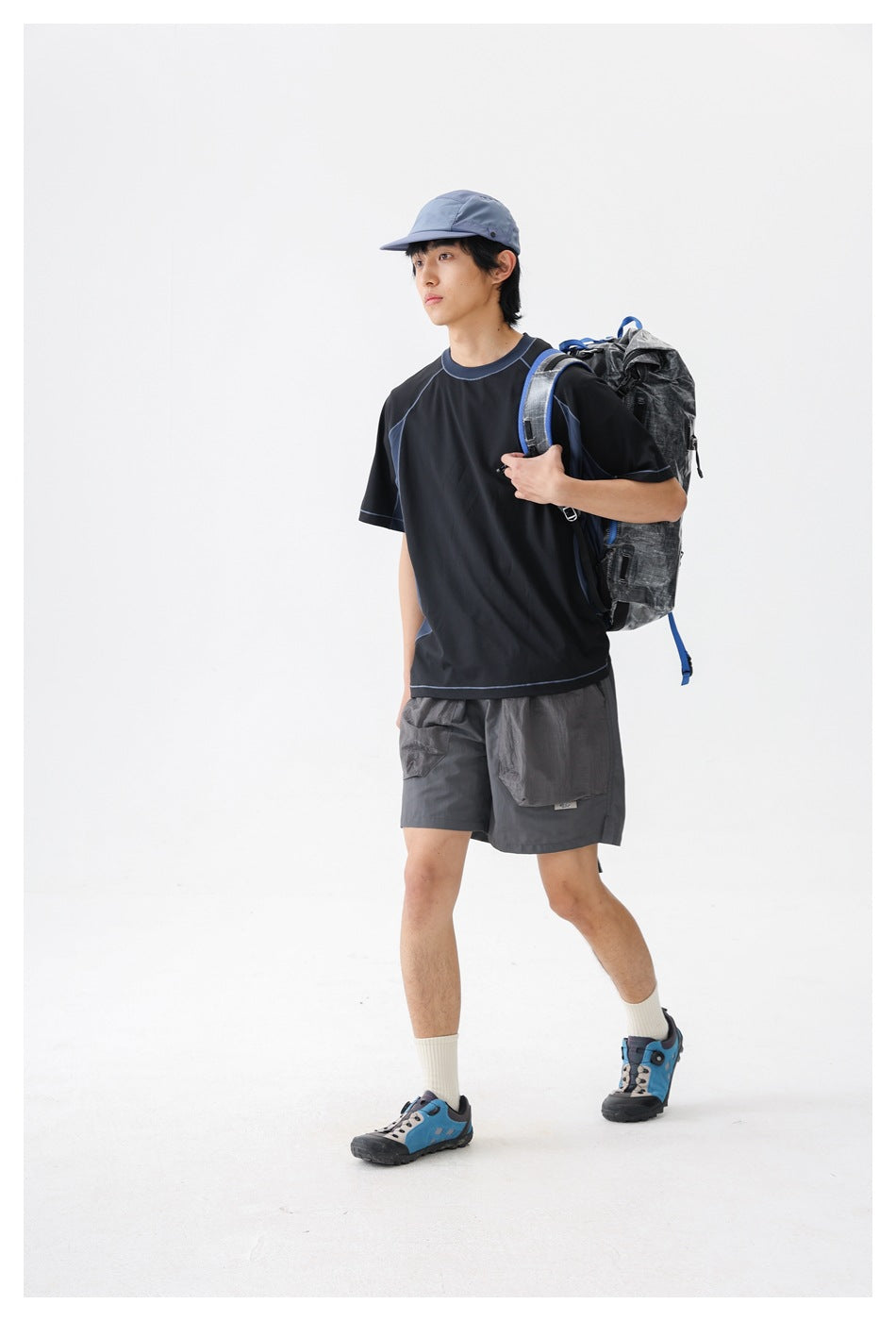 Model wearing a black short-sleeve top with blue contrast piping and dark gray cargo shorts.