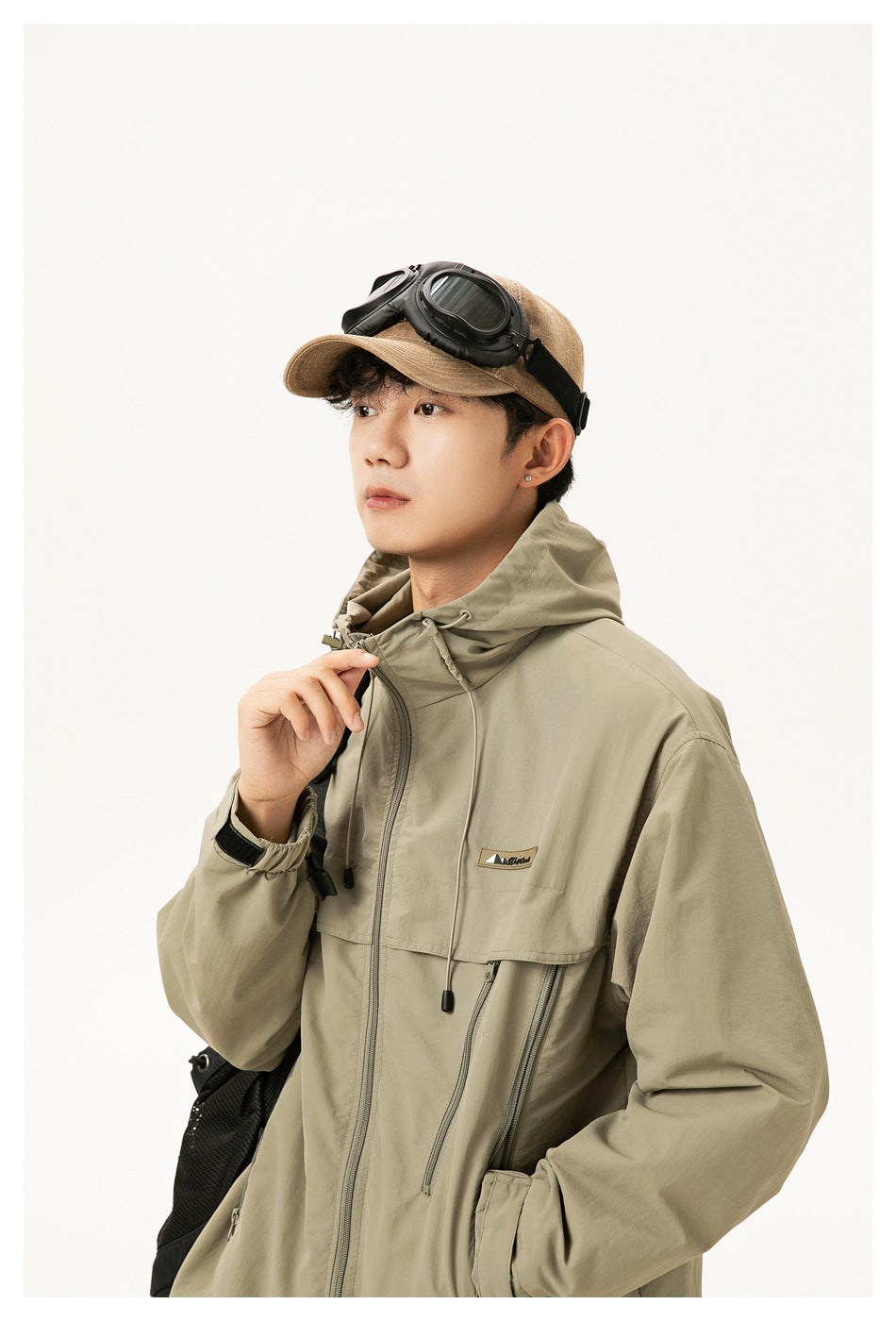 Man wearing a khaki hooded jacket with a front zipper, chest flap and zip pockets.