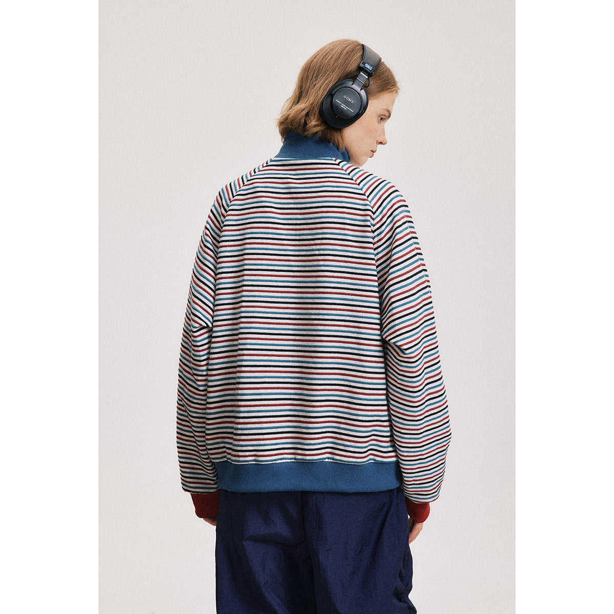 Back view of a model wearing a striped jacket with a blue collar and hem, red cuffs, and navy pants.