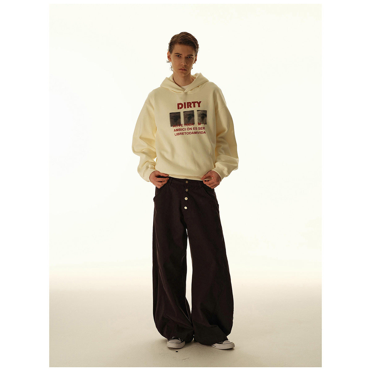 Model wearing a cream graphic hoodie and extremely wide black button-front trousers, shown full length.