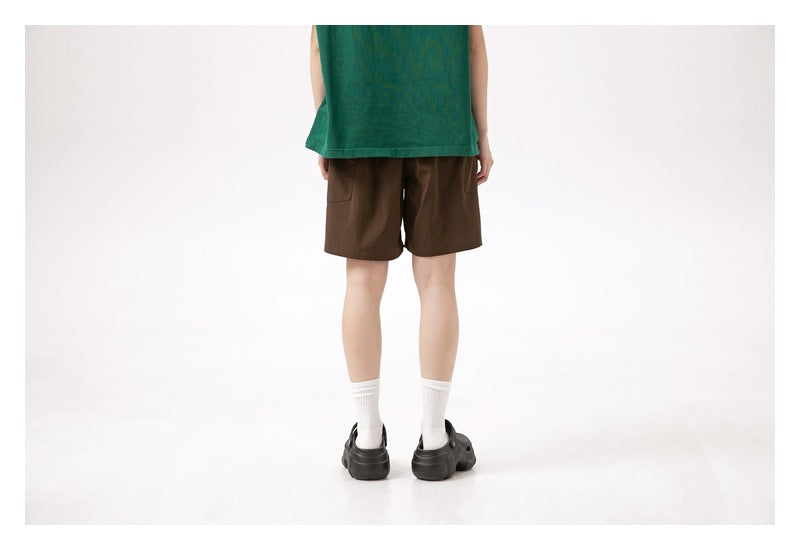 Back view of a model wearing brown shorts with a green T-shirt, white socks, and black clogs.
