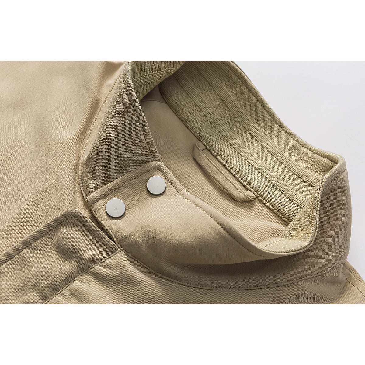 Close-up of a tan jacket's ribbed collar, inner snap-button tab, and stitching.