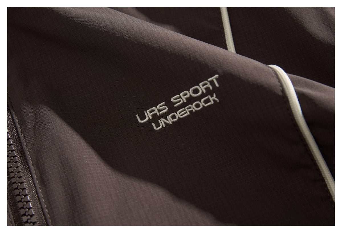 Close-up of dark brown garment fabric with white embroidered lettering, cream piping and a black zipper.