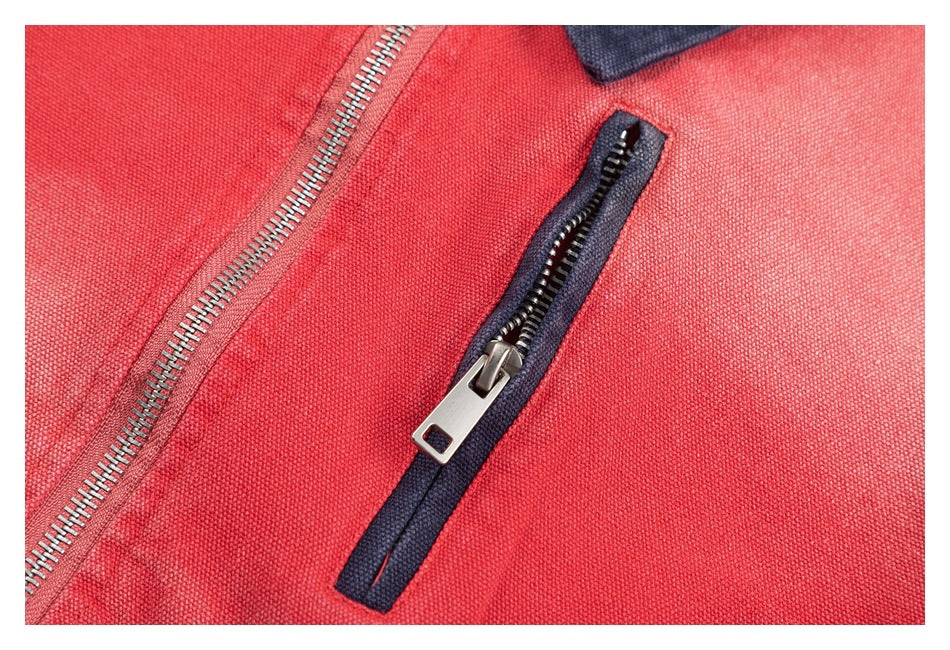 Close-up of a coral-red jacket showing a dark-trimmed zip pocket beside the silver front zipper.