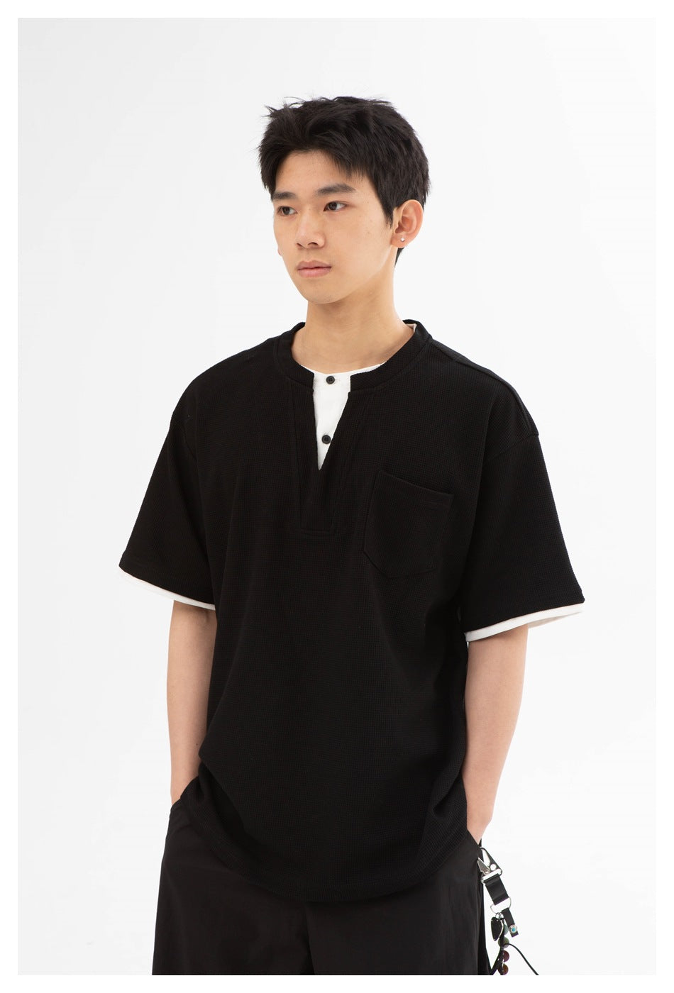 Closer front view of a man wearing a black textured short-sleeve henley with white trim and a chest pocket.