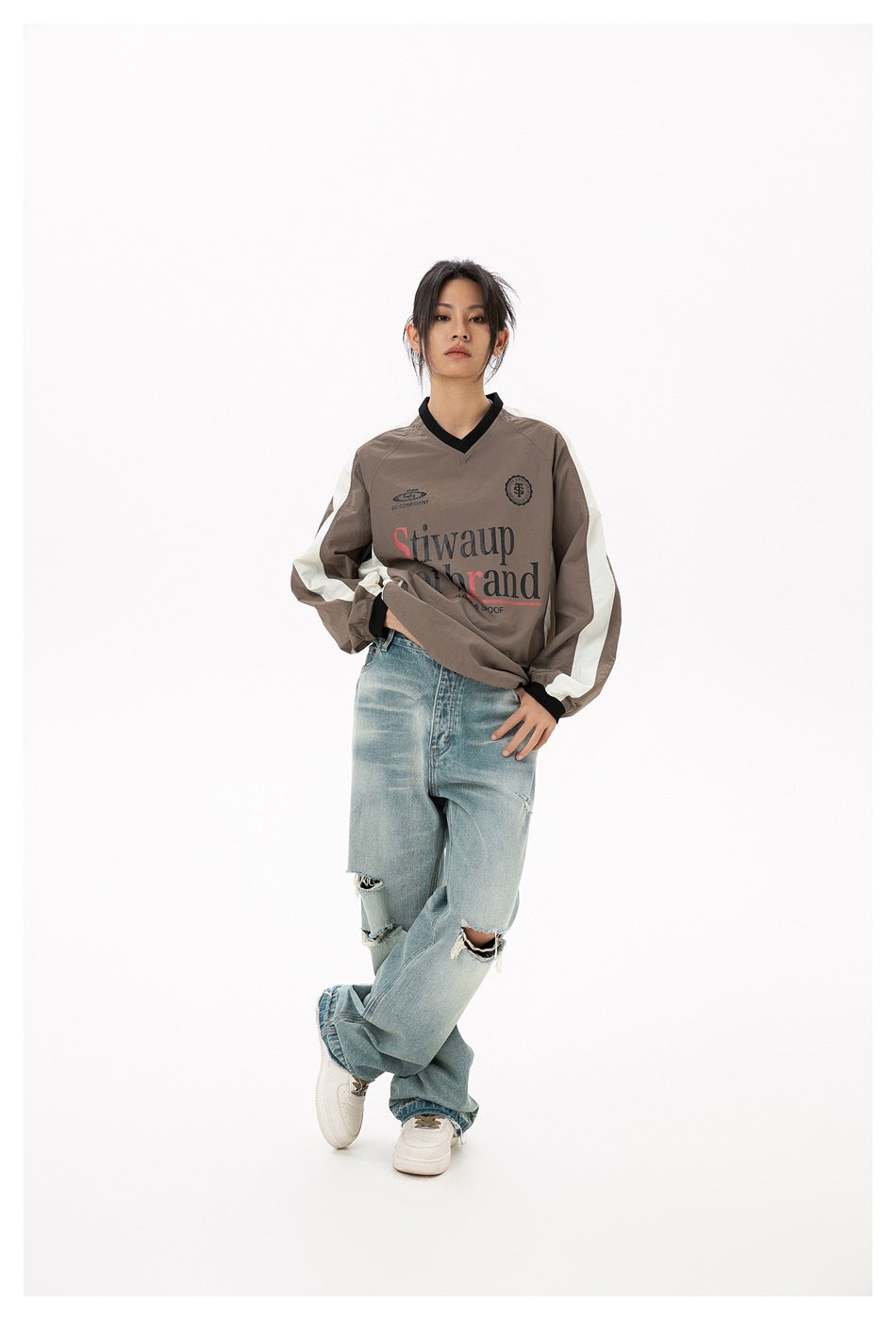 Person wearing the light brown V-neck top with cream sleeve stripes and chest print, styled with ripped light-wash jeans