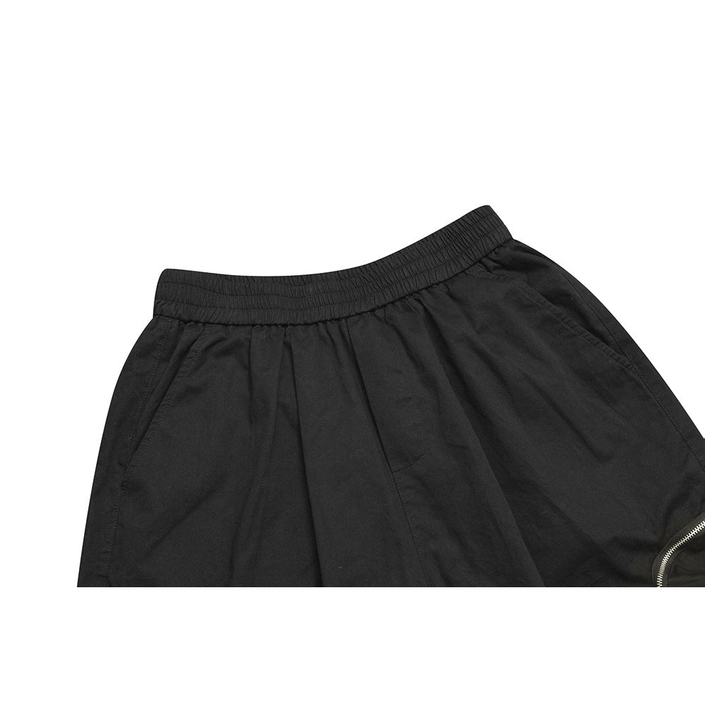 Close-up of black pants showing the elastic waistband, front pocket seam, and part of a silver zipper.