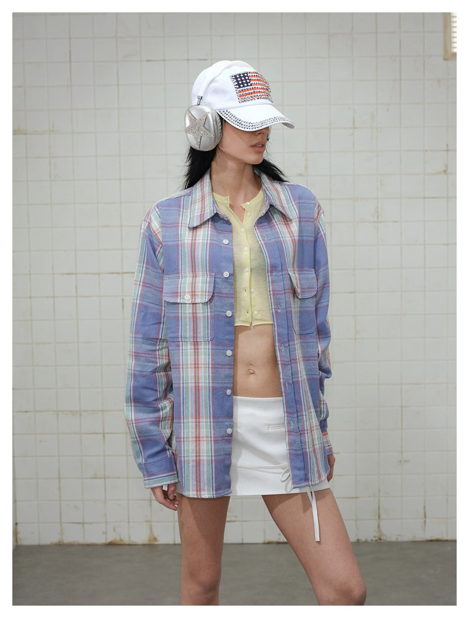 Model wearing a blue plaid button-up shirt over a pale yellow cropped top and white skirt, with a white cap and silver