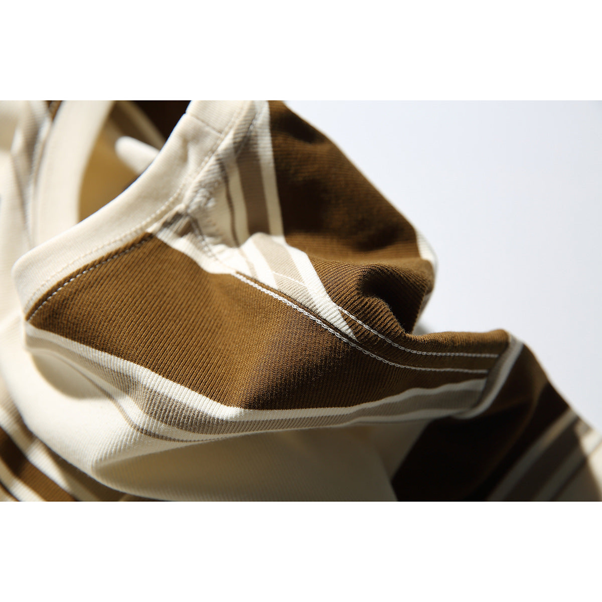 Close-up of cream, brown, and taupe striped fabric with a visible seam and stitching.