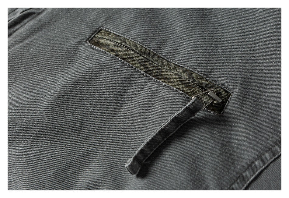 Close-up of a narrow olive-patterned welt pocket and hanging fabric tab on a gray jacket.