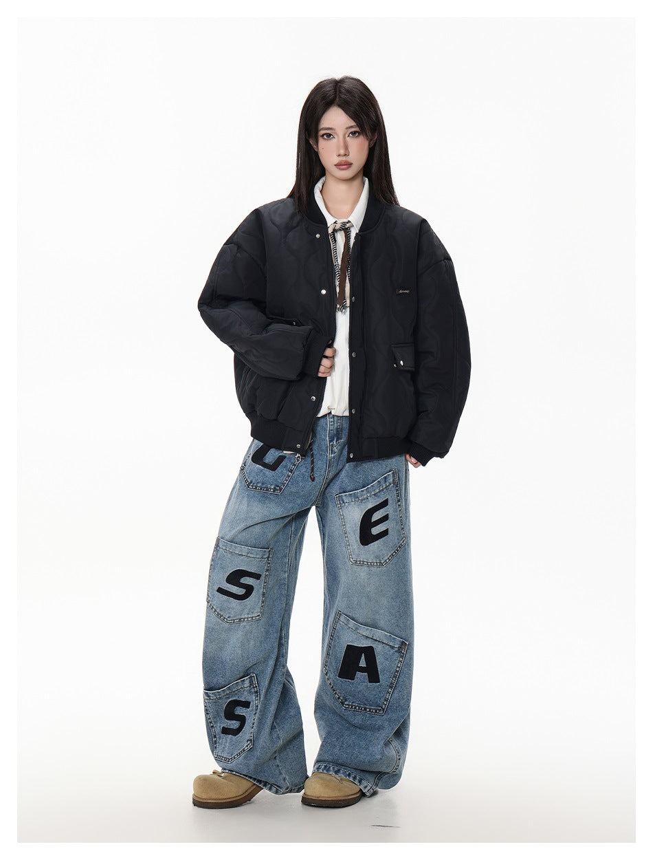 Model wearing a black quilted snap-front bomber jacket with ribbed trim and oversized blue patchwork jeans.