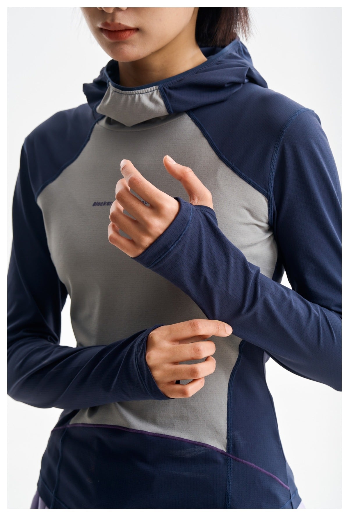Close-up detail of a navy and gray hooded top, showing its hood, seams, and thumbhole sleeve cuffs.