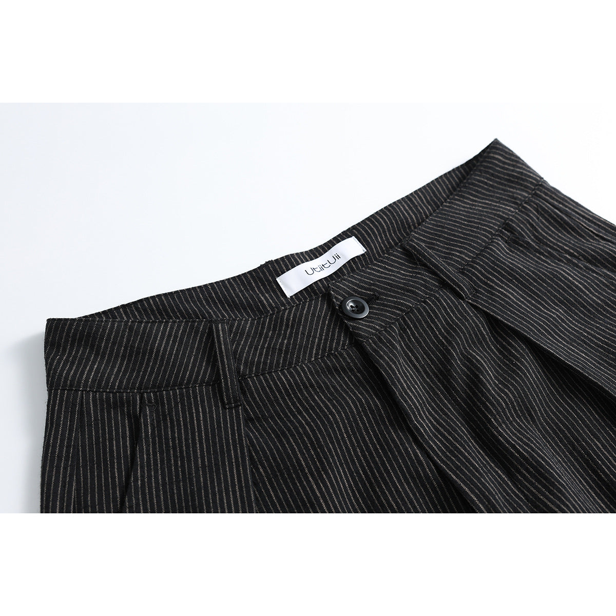 Close-up of dark pinstriped trousers showing the waistband, pleats, button, and inner label.