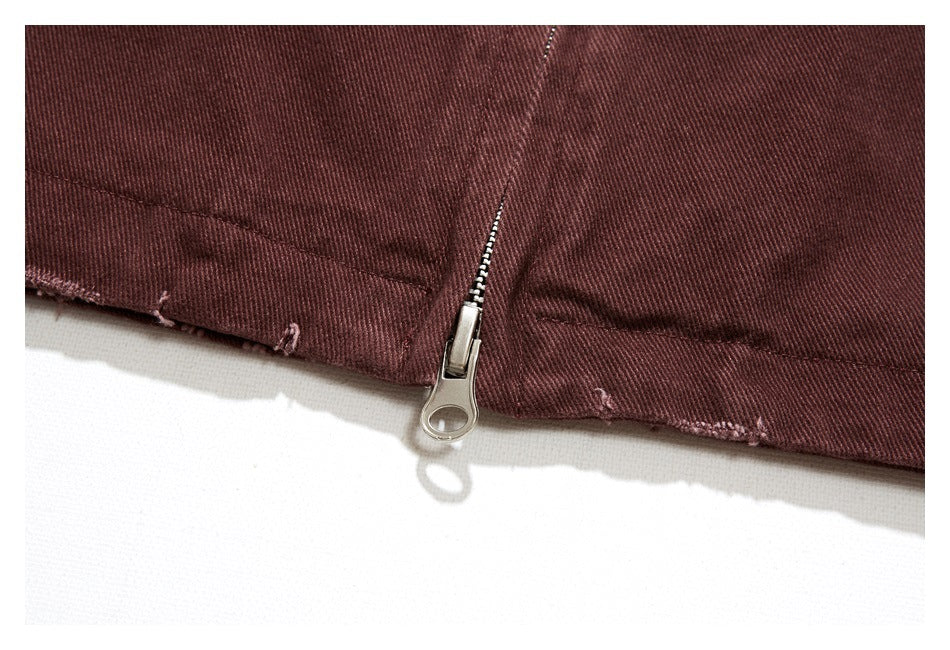 Close-up of a metal zipper at the hem of a burgundy jacket, with lightly frayed edges.