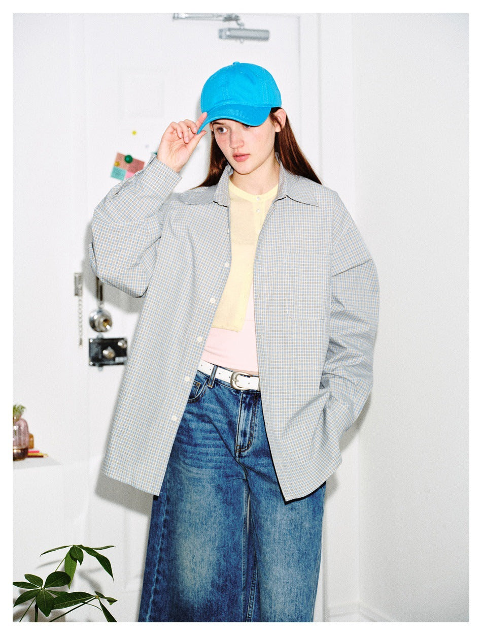 Front view of a model in an oversized gray-blue plaid button-up shirt, blue cap, and wide-leg jeans.