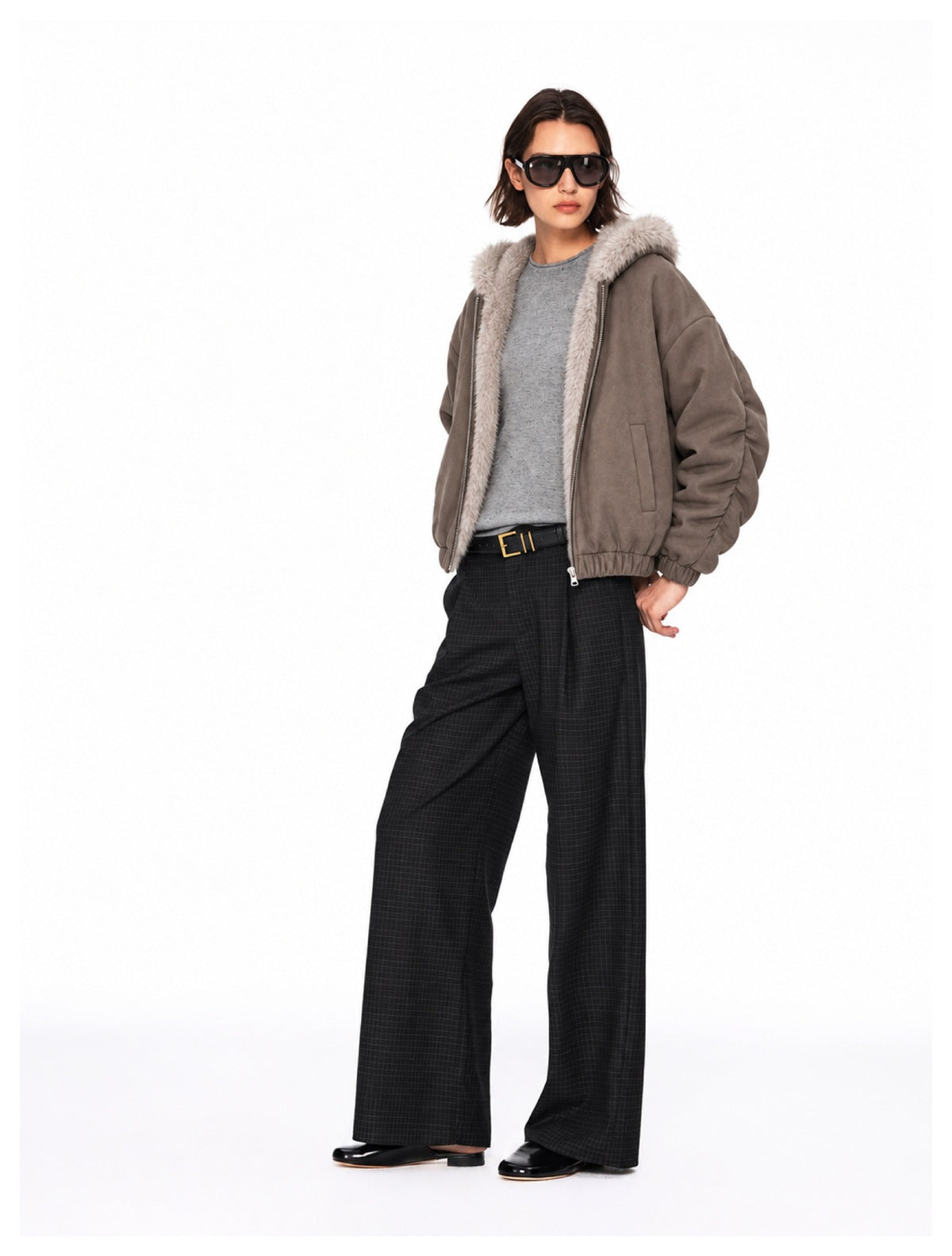 Model wearing an open taupe fur-trimmed hooded jacket with wide-leg checked trousers.