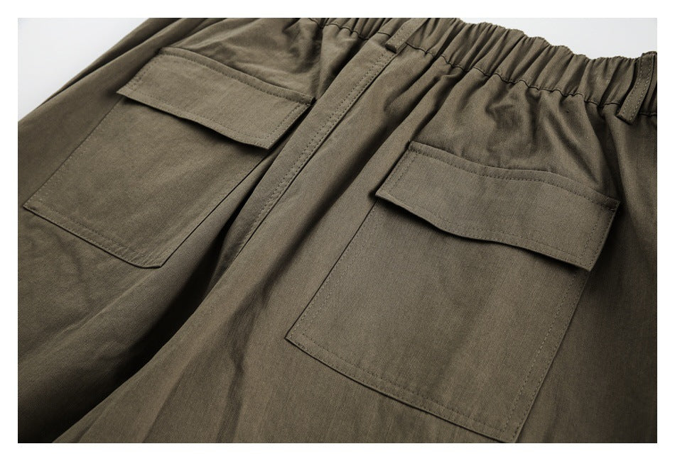 Close-up of olive-brown trousers showing two large flap pockets beneath a gathered waistband.