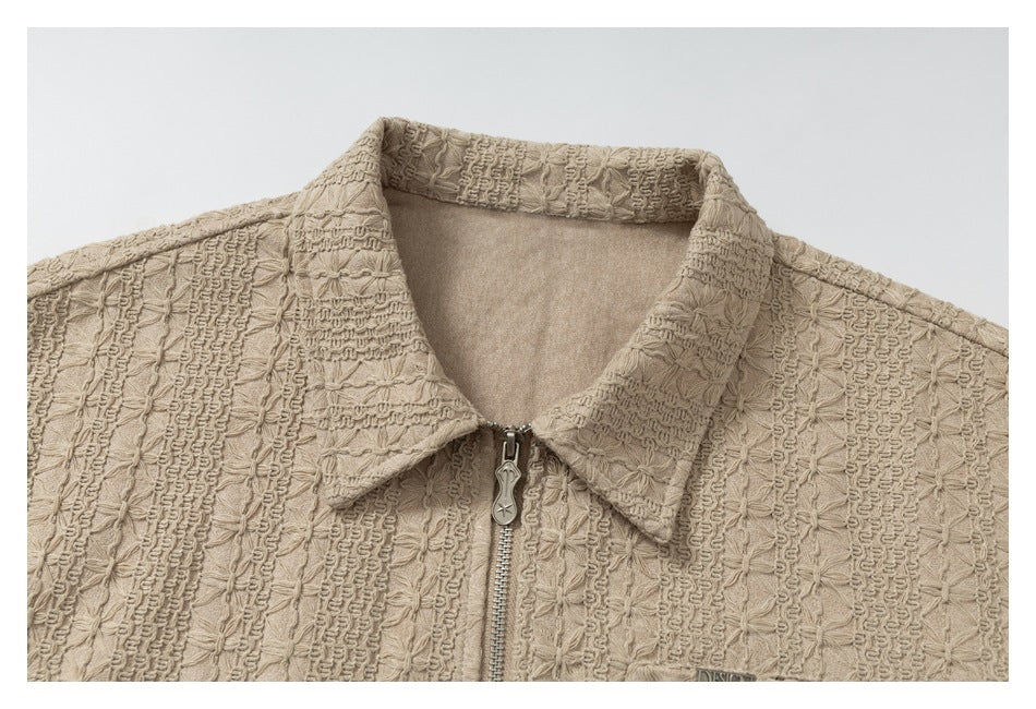 Close-up of the beige jacket's textured fabric, pointed collar and metal front zipper.
