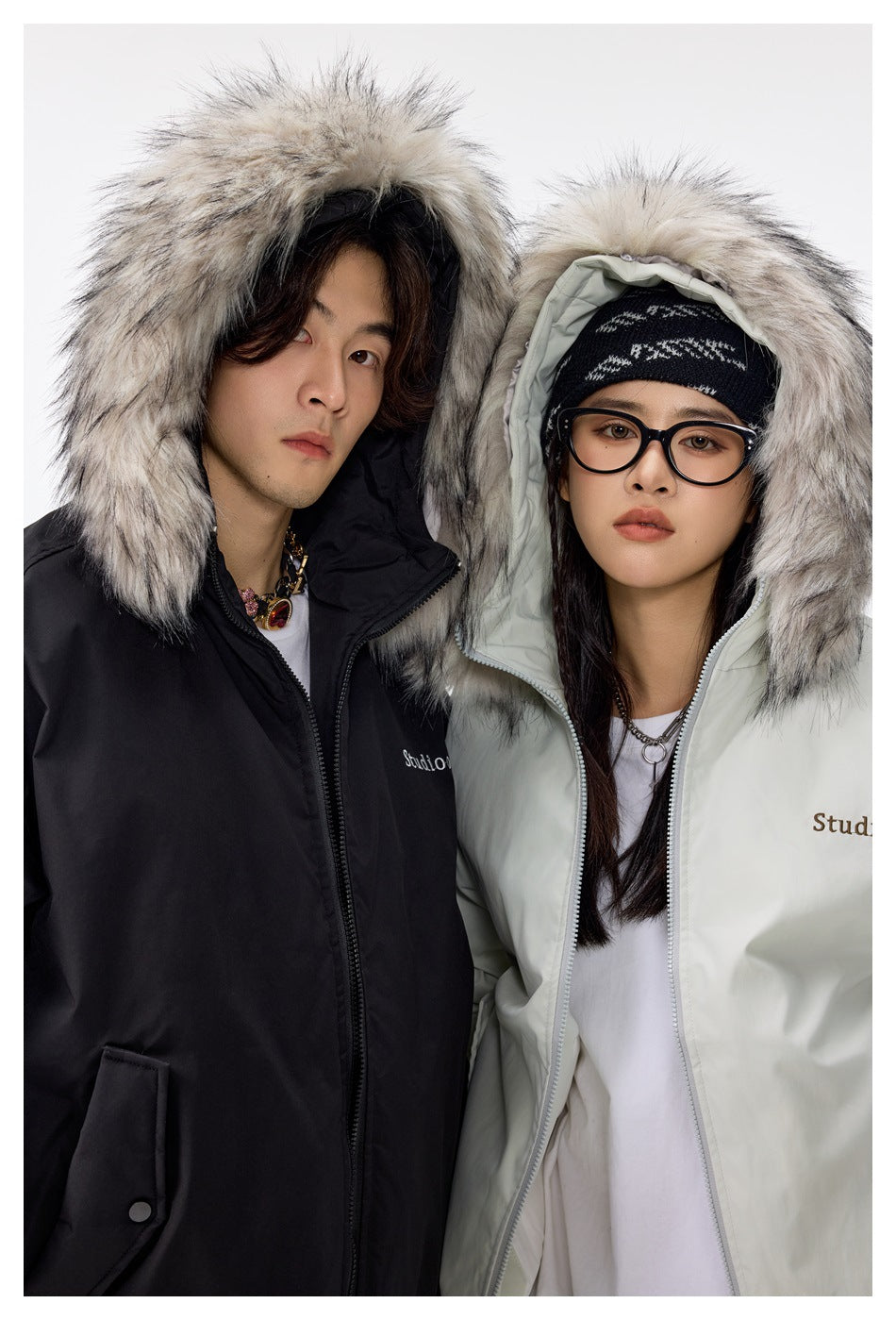 Close-up of two models in black and light green jackets with hoods up showing large fur-style trim
