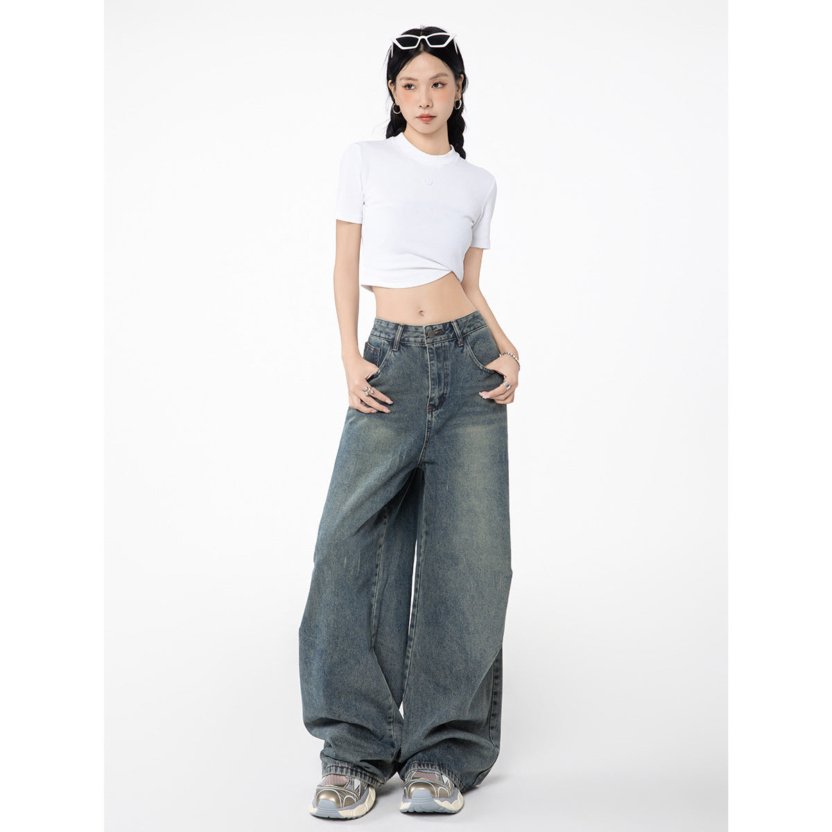 Model wearing a white cropped T-shirt and very wide-leg faded blue jeans, full-length front view.