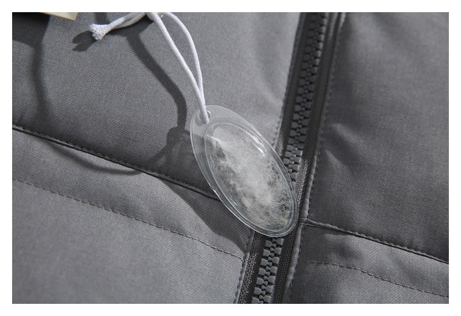 Close-up of gray garment fabric, a dark zipper, and a clear oval tag containing a feather.