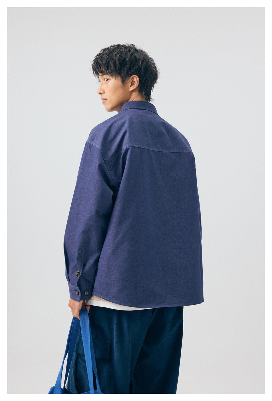Rear view of a model wearing a blue button-up shirt and dark cargo pants.