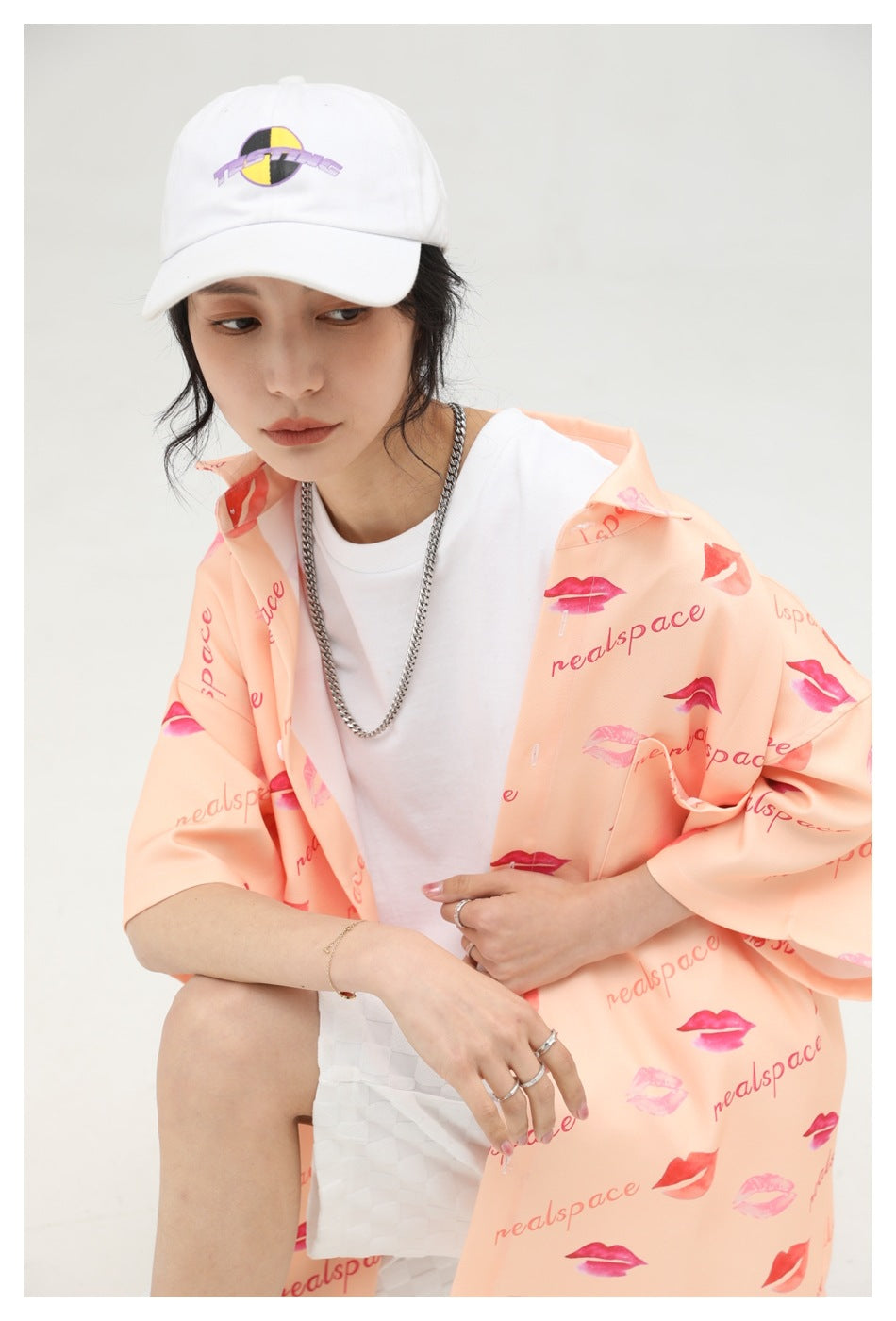 Model wearing a peach short-sleeve button-up shirt with lipstick prints and lettering over a white T-shirt.