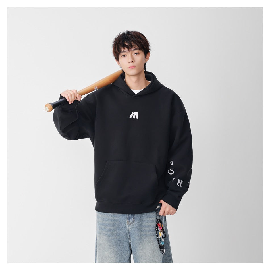 Model wearing a black oversized hoodie with a white chest emblem and sleeve lettering, paired with light-wash jeans.