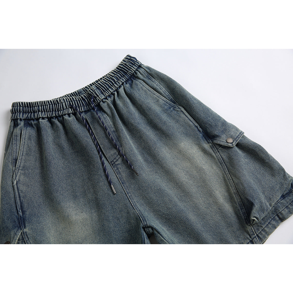 Cropped front view of blue-gray denim shorts with an elastic drawstring waist and buttoned side flap pocket.