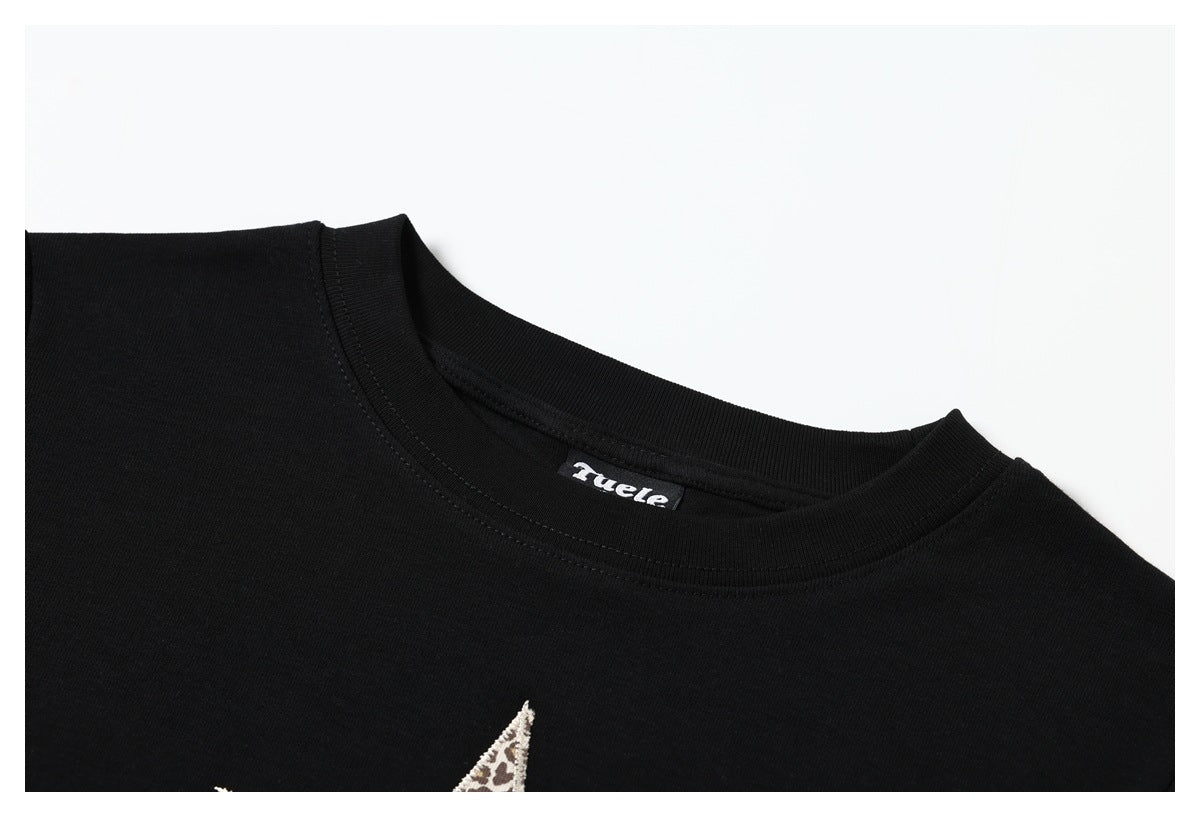 Close-up of the black T-shirt's crew neckline, with a sewn neck label and part of a decorative chest motif.