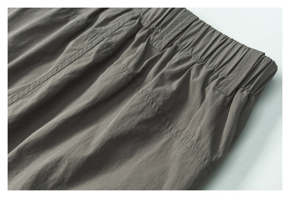 Close-up of charcoal-gray trousers showing the gathered waistband, belt loops, and stitching.