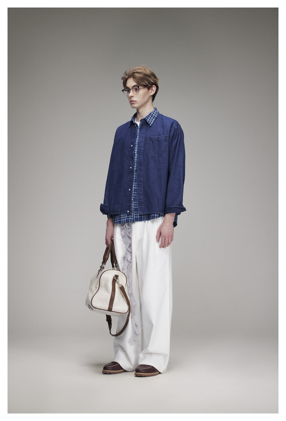 Three-quarter view of a model in a blue denim overshirt with plaid trim and white wide-leg trousers.