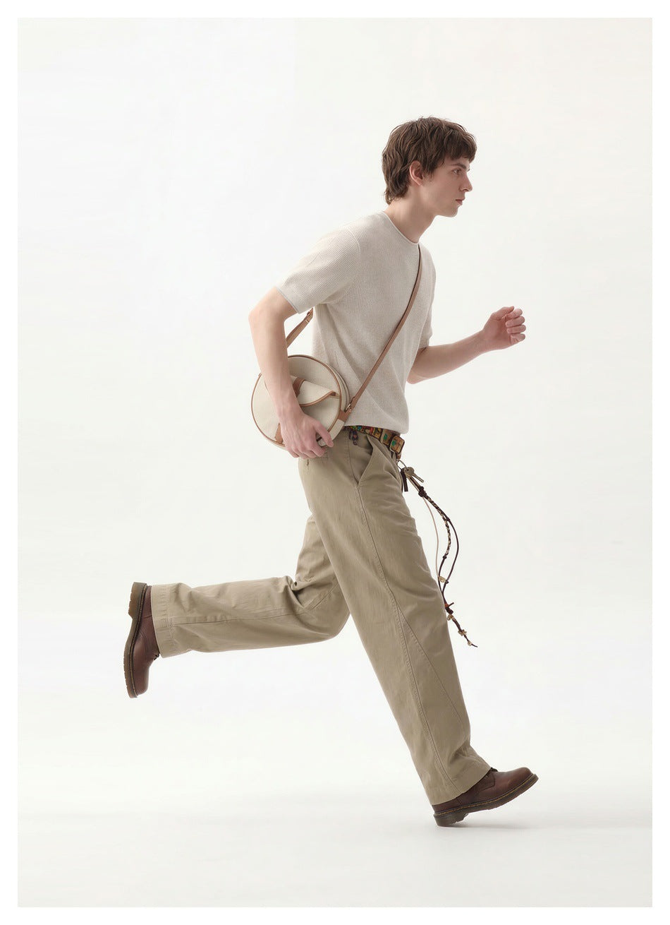 Model running in an off-white short-sleeve crewneck top and khaki trousers, with a cream crossbody bag.