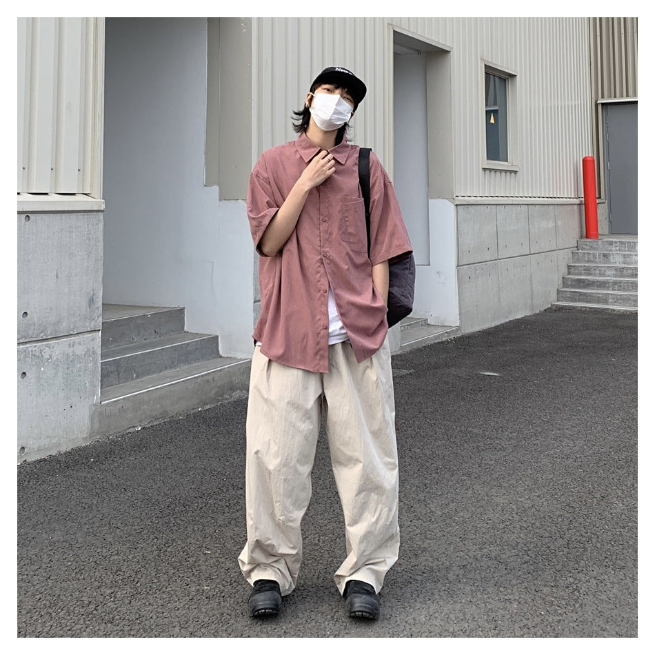 Person wearing a dusty rose short-sleeve button-up shirt with a chest pocket and loose cream pants.