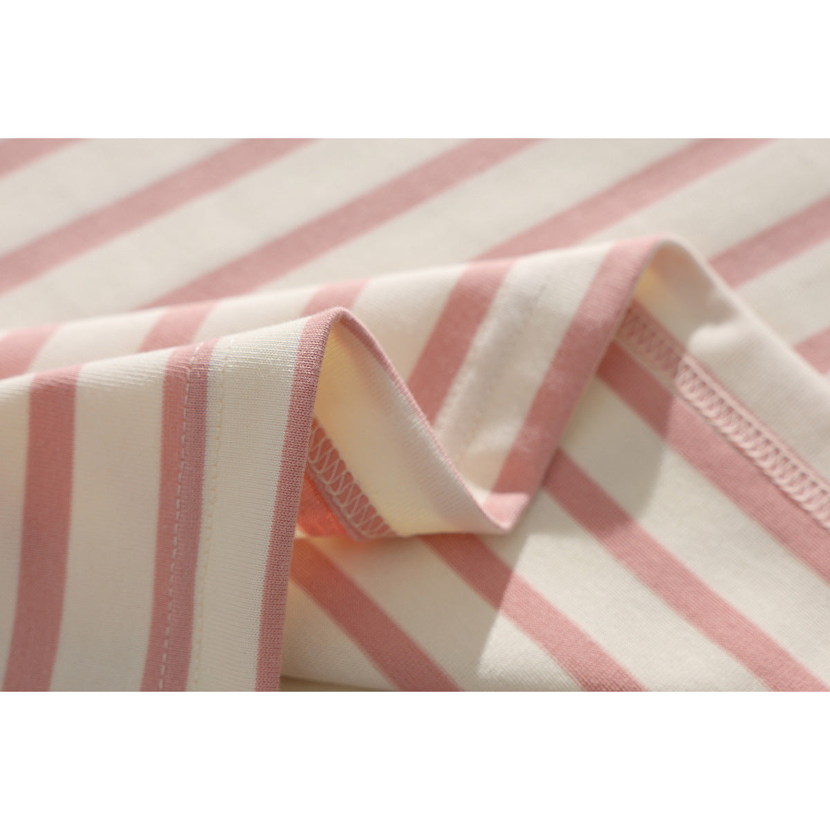Close-up of cream and dusty pink striped T-shirt fabric folded to show its stitched edge and overlocked seam.