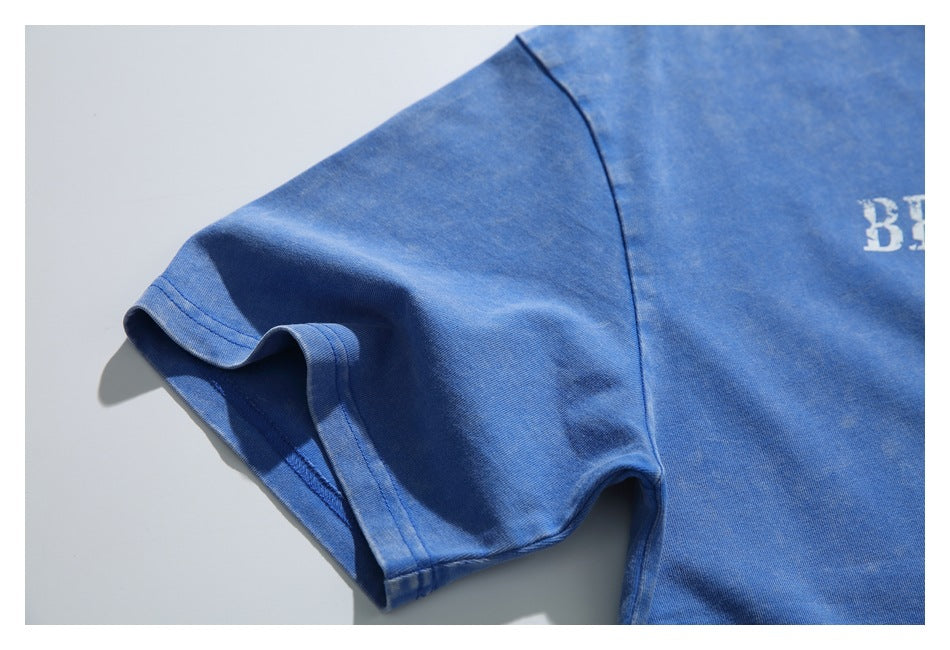 Close-up of a blue T-shirt's short sleeve, sleeve hem and shoulder seam; partial white print appears at the edge.