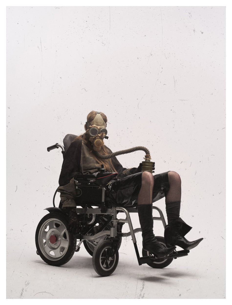 Model seated in a powered wheelchair wearing a camouflage raglan top with black sleeves and black shorts.
