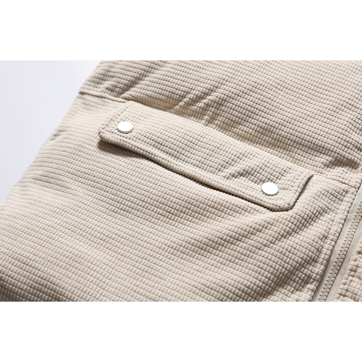 Close-up of the cream jacket's textured fabric and flap pocket with two snap closures.