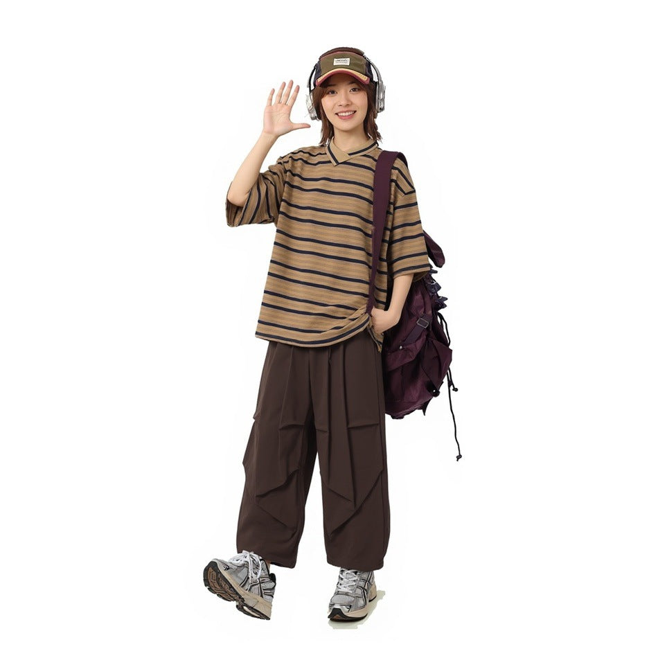 Model wearing the brown navy-striped T-shirt with brown wide-leg pants, cap, headphones and a purple backpack