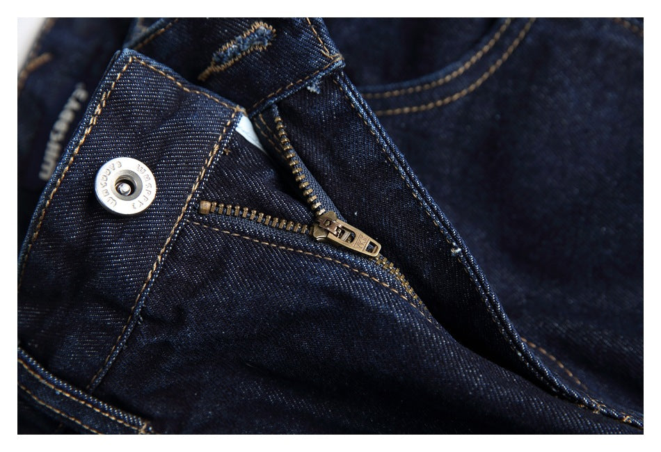 Close-up of the jeans' open fly, zipper and metal waistband button in dark indigo denim.