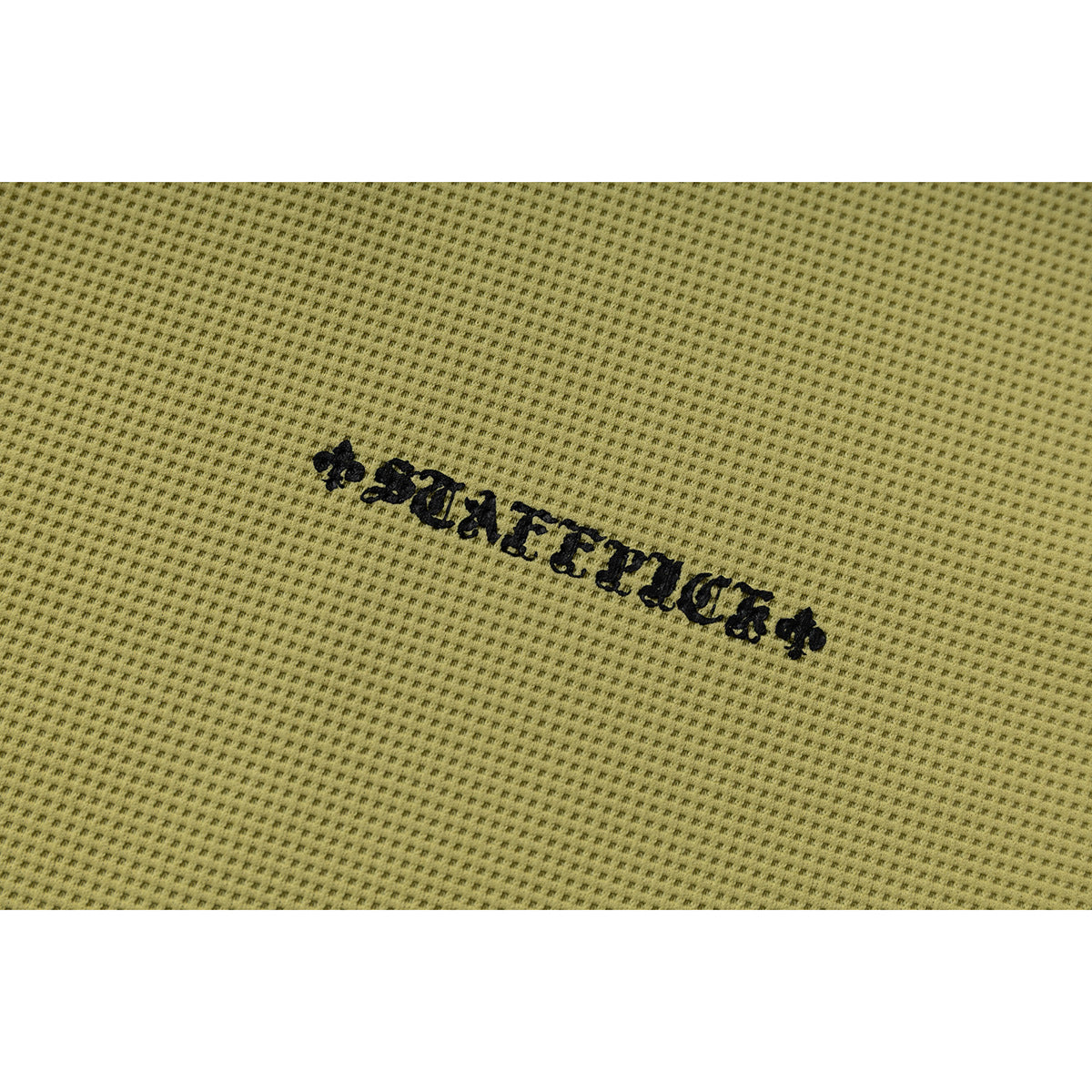 Close-up of black decorative lettering embroidered on muted olive-yellow textured fabric.