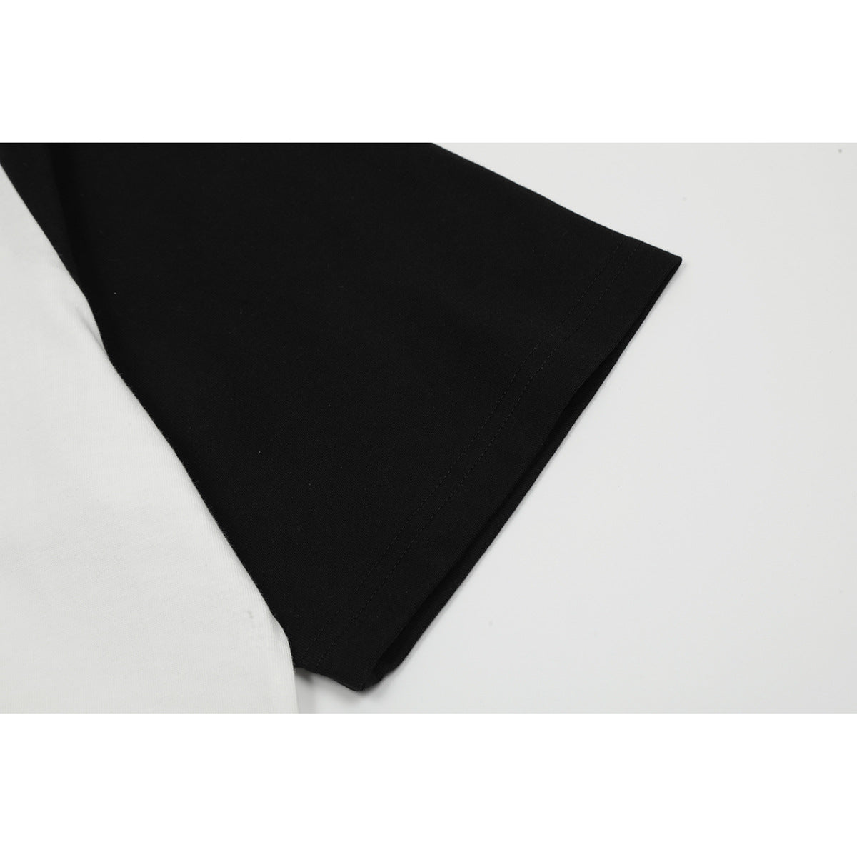 Close-up of a black short sleeve and stitched edge beside the white body of a raglan T-shirt.
