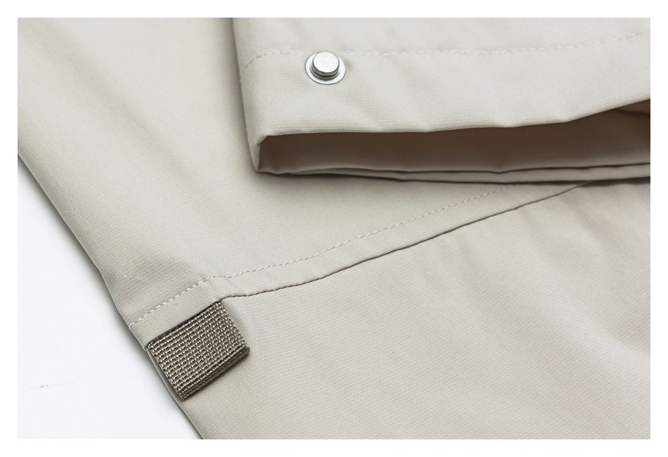 Close-up of a light beige garment cuff with a metal snap, stitched seam, and fabric tab.