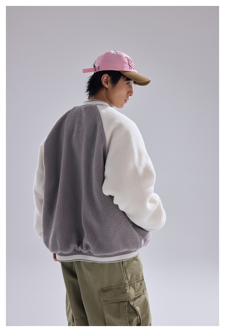 Model turned away to show the back of a gray-and-white color-block fleece varsity jacket.